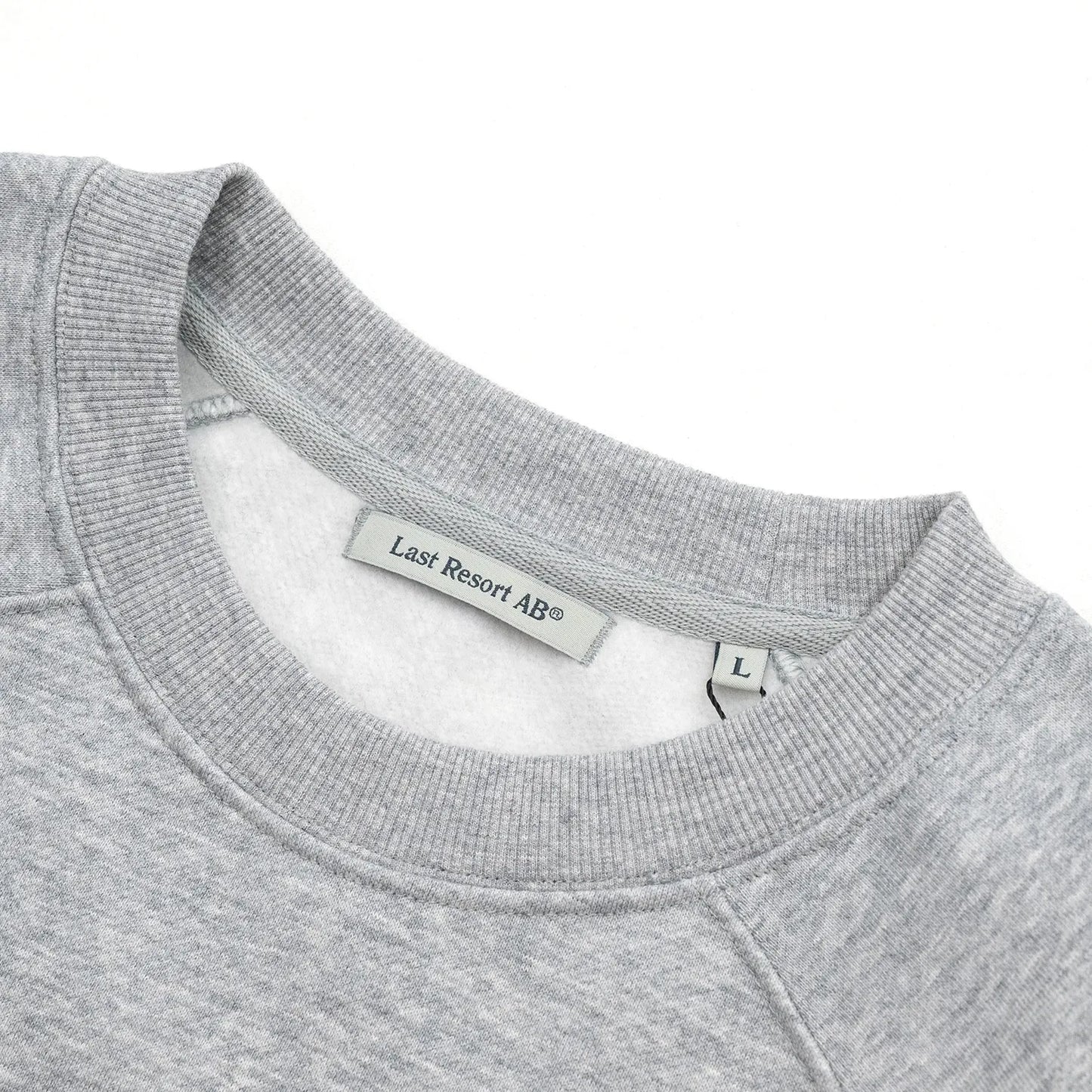 LAST RESORT AB(ラストリゾート)のアトラスロゴが左胸にプリントされたスエット「LITTLE AB RAGLAN CREW SWEAT」の「GREY MELANGED」カラーの襟元の写真