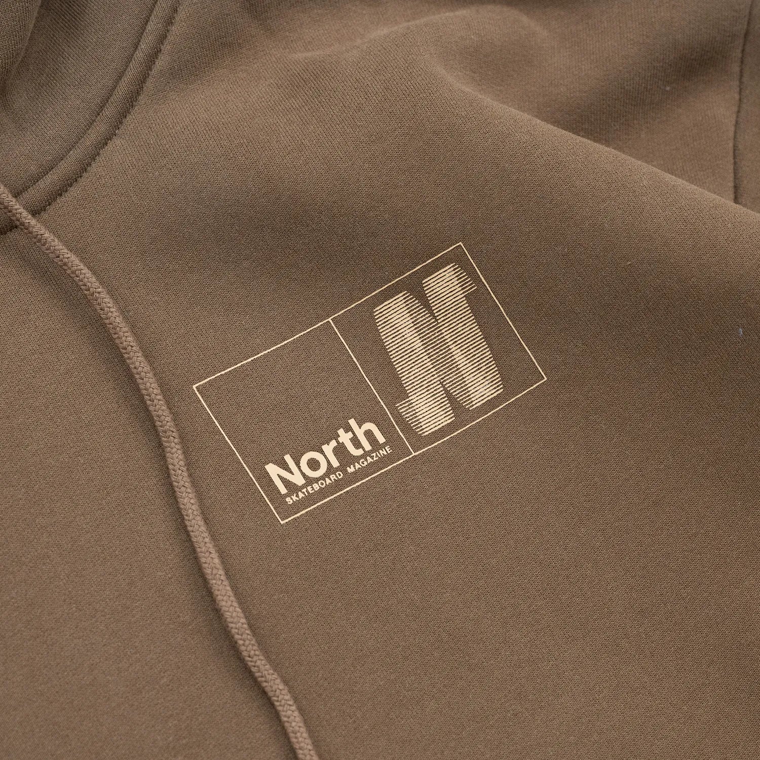 NORTH SKATE MAG(ノーススケートマグ)のバック大きく、フロント左胸にワンポイントでデザインがプリントされた肉厚なパーカー「N LOGO HOODIE」のBROWNカラーの襟元の写真