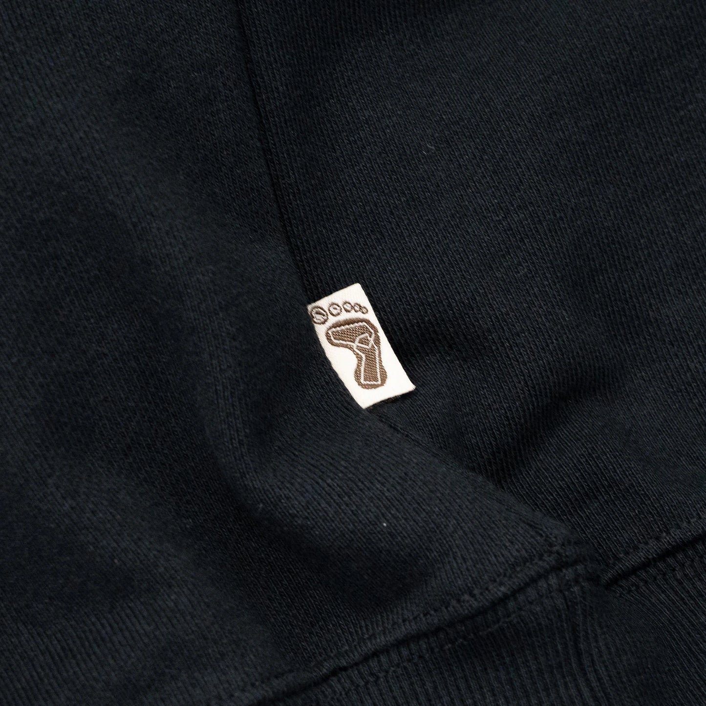 TRIBE WEAR(トライブウェア)の肉厚なフーディー|パーカー「BASIC HOODIE」のBLACKカラーの左脇下のブランドタグ写真