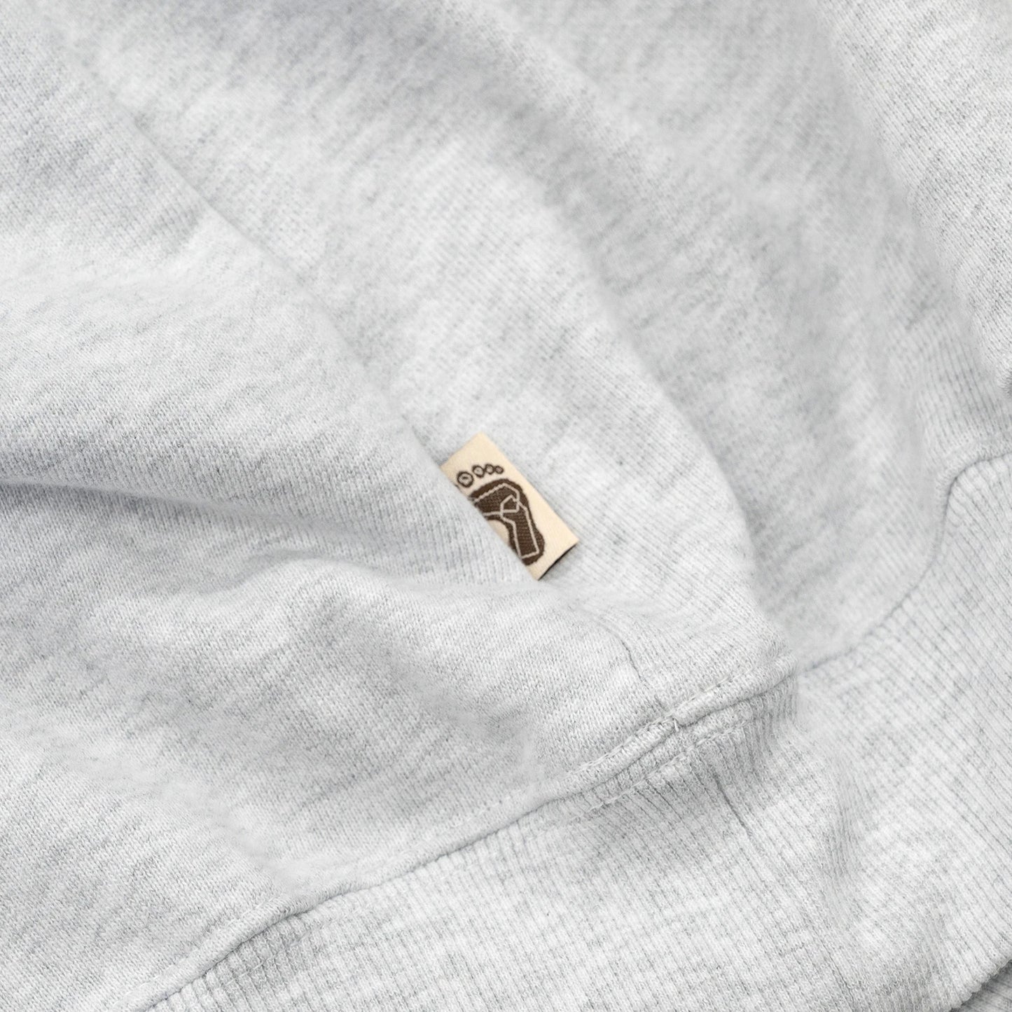 TRIBE WEAR(トライブウェア)の肉厚なフーディー|パーカー「BASIC HOODIE」のGREYカラーの左脇下のブランドタグ写真