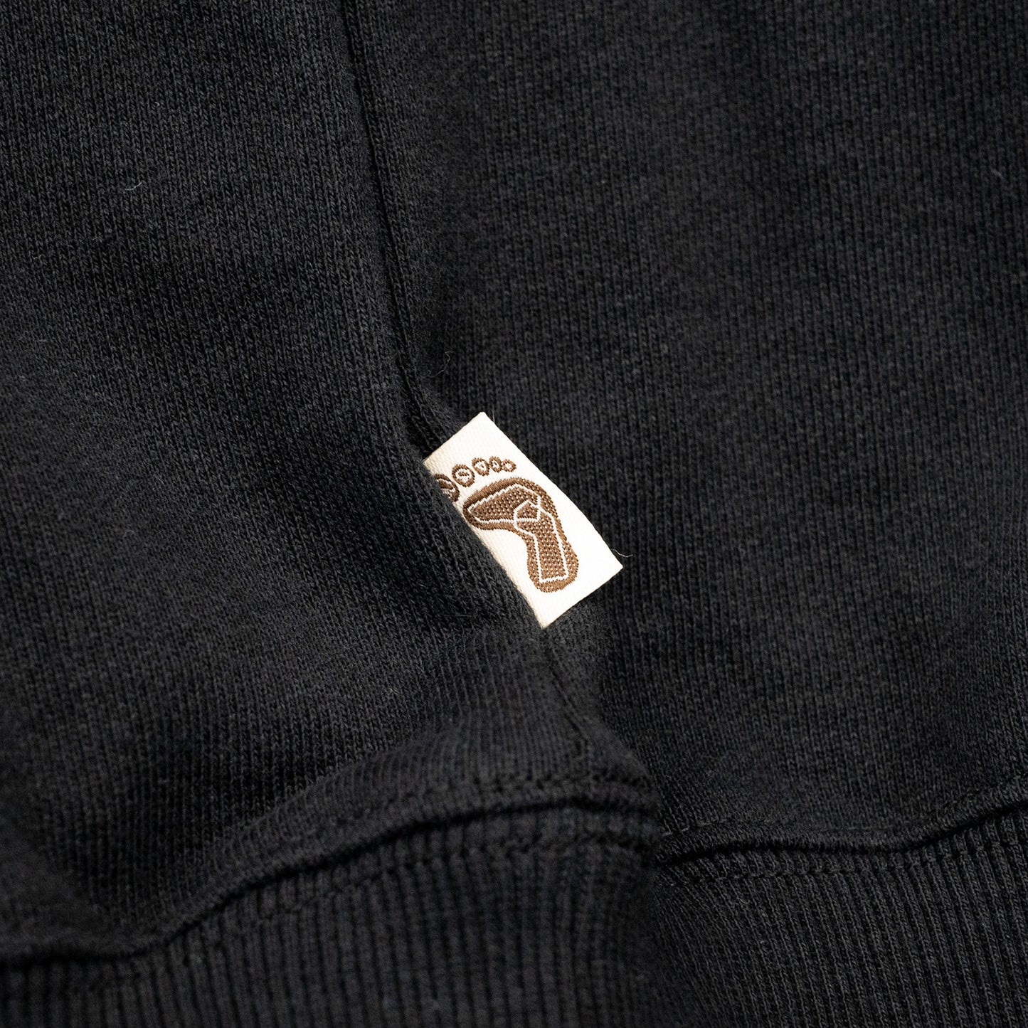 TRIBE WEAR(トライブウェア)の肉厚な生地感とファットなシルエットのクルーネックスエット「BASIC SWEAT CREWNECK」のBLACKカラーの左脇下のブランドタグの写真