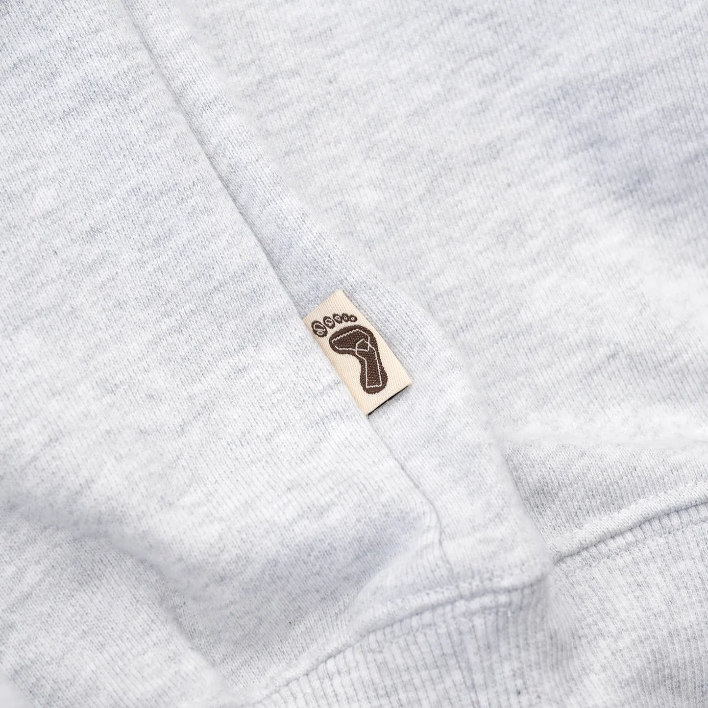 TRIBE WEAR(トライブウェア)の肉厚な生地感とファットなシルエットのクルーネックスエット「BASIC SWEAT CREWNECK」のGREYカラーの左脇下のブランドタグの写真
