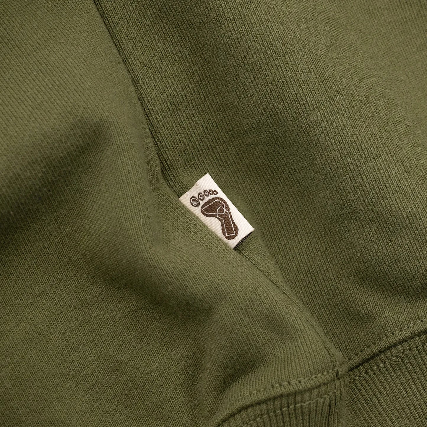 TRIBE WEAR(トライブウェア)の肉厚な生地感とファットなシルエットのクルーネックスエット「BASIC SWEAT CREWNECK」のOLIVEカラーの左脇下のブランドタグの写真