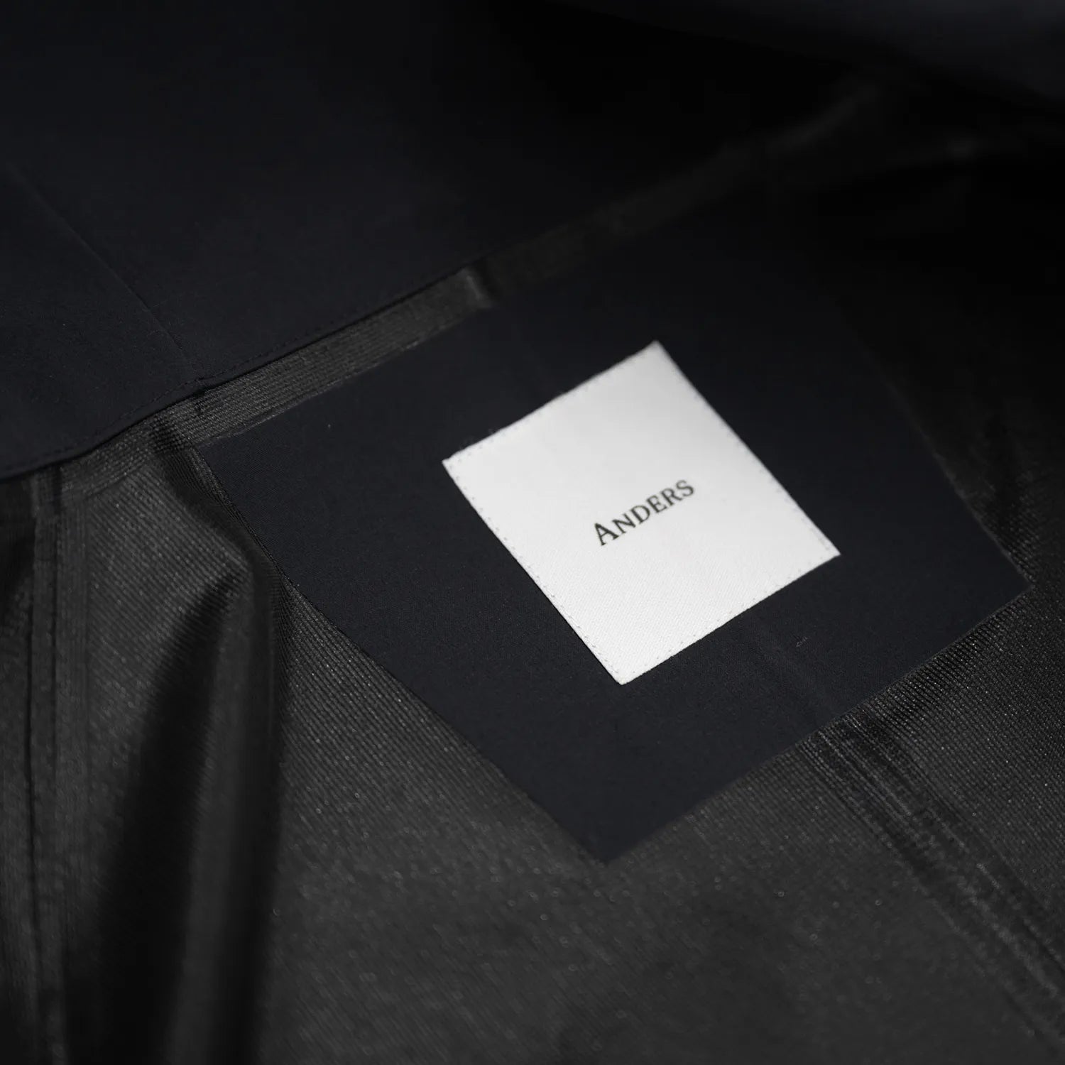 米軍の「ECWCS LEVEL6 JACKET GEN1 後期型」をベースにAndersが再構築したの3LAYERコート「3LAYERS ECWCS HARD SHELL COAT」のMATT BLACKカラーの襟裏ブランドロゴの写真
