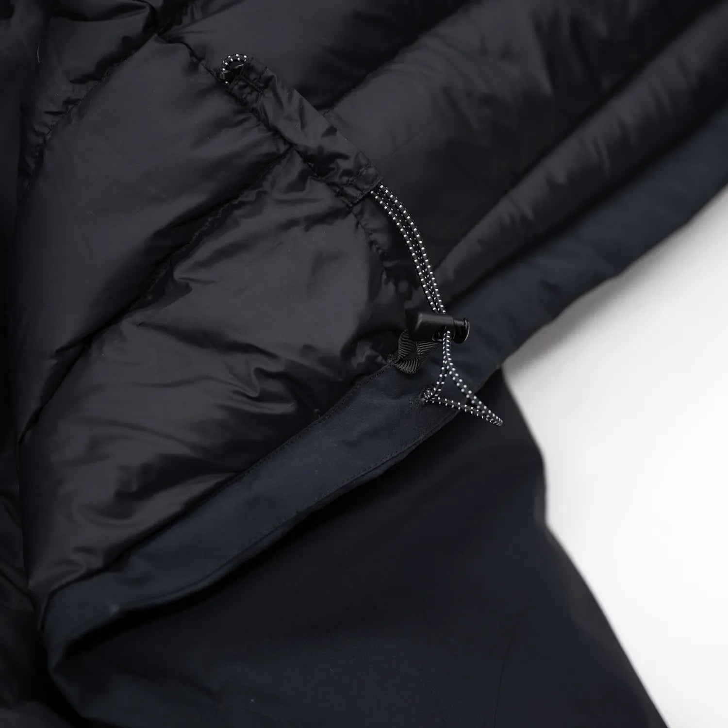 米軍の「ECWCS LEVEL6 JACKET GEN1 後期型」をベースにAndersが再構築したのハードシェル・パファージャケット「3LAYERS ECWCS HARD SHELL PUFFER JACKET」のMATT BLACKカラーの裾脇のドローコードの写真