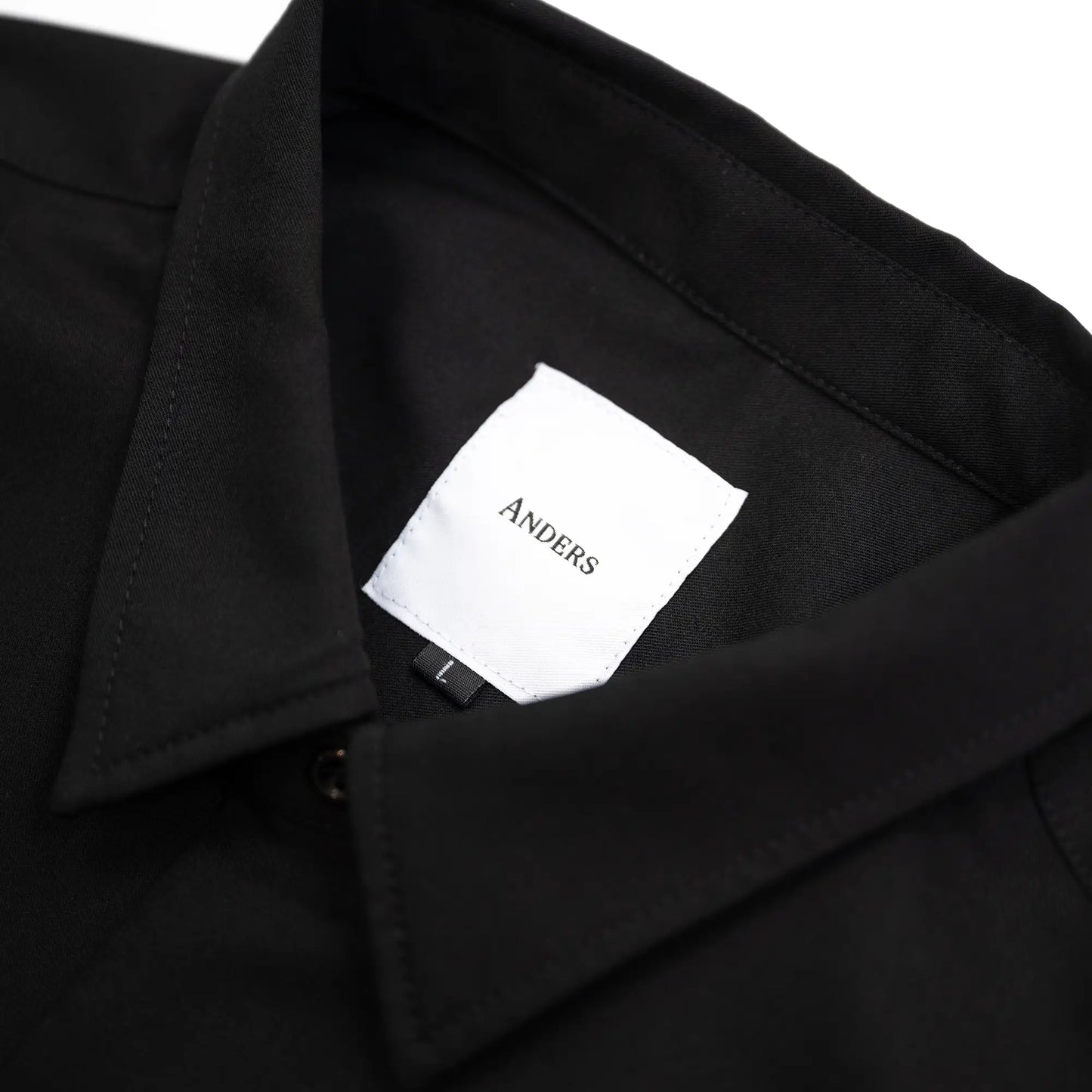 考え抜かれたワイドなボックスシルエットのAndersの傑作ドレープシャツ「WIDE DRAPE S/S SHIRTS」の「CROW」カラーの襟裏のブランドタグ写真