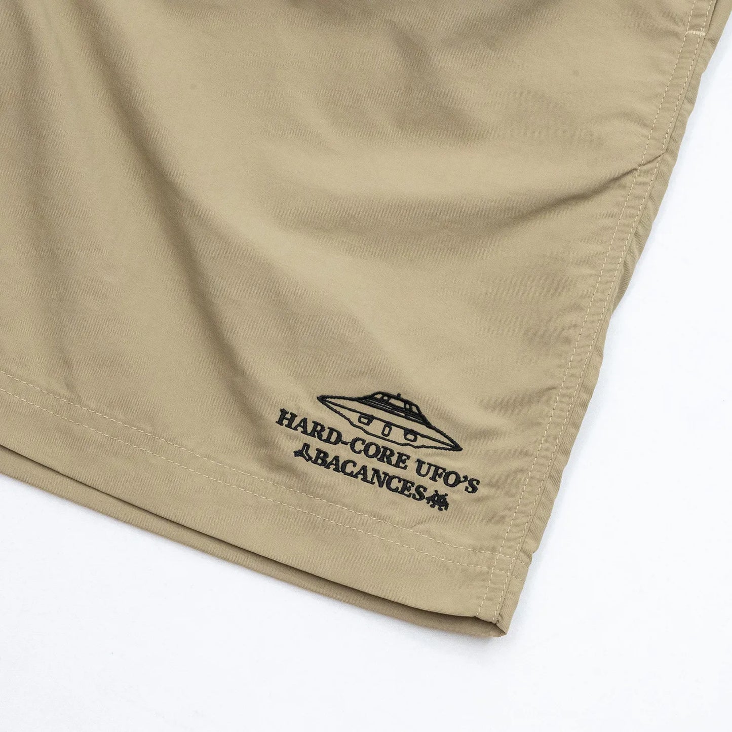 BACANCESのナイロン製の水陸両用ショーツ「BC NYLON SHORTS HARDCORE UFO'S LOGO」のCOYOTEカラーの左裾の刺繍デザインの写真