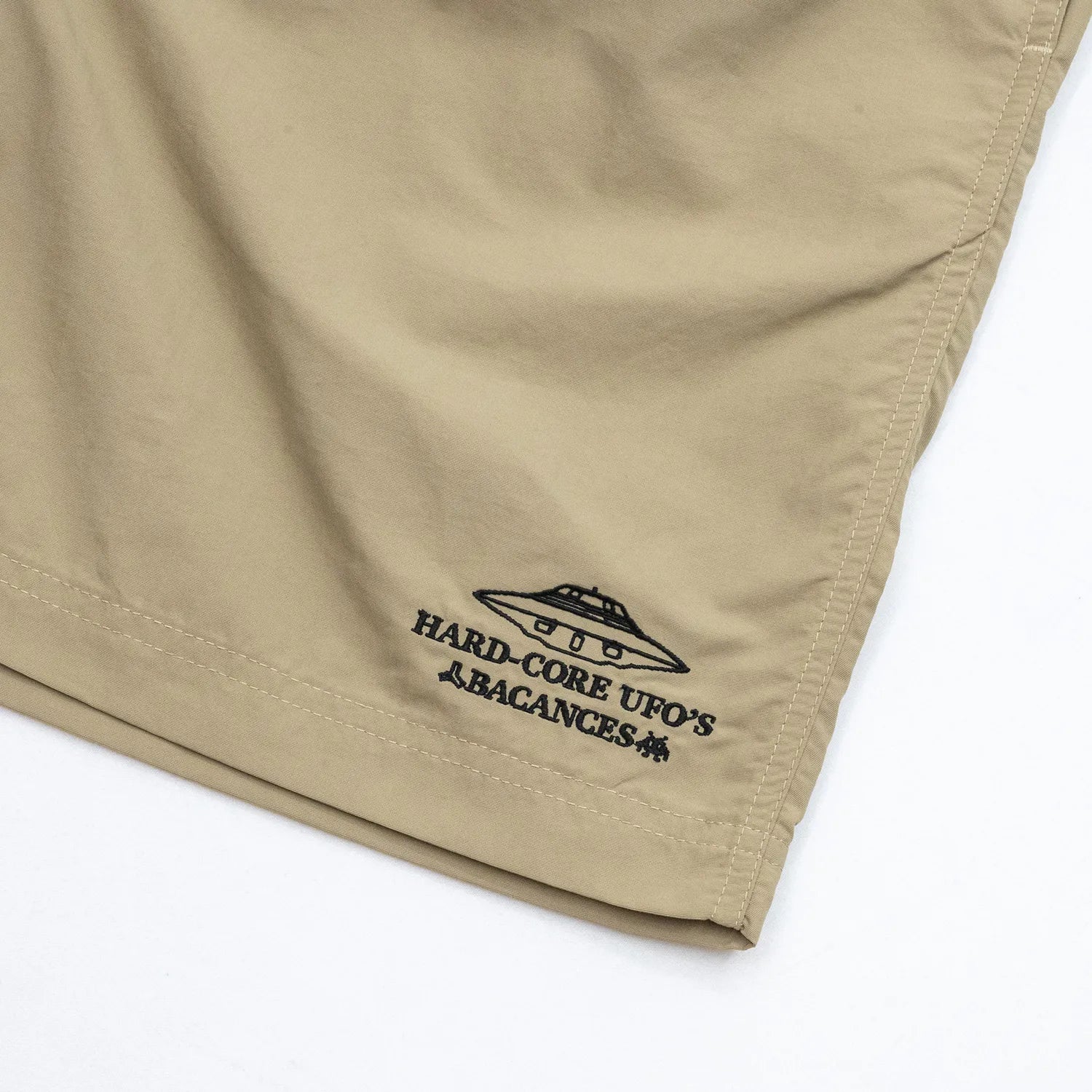 BACANCESのナイロン製の水陸両用ショーツ「BC NYLON SHORTS HARDCORE UFO'S LOGO」のCOYOTEカラーの左裾の刺繍デザインの写真