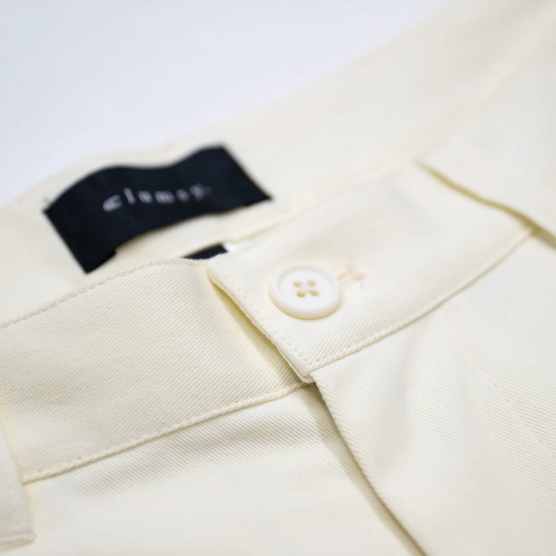 clumsy. PICTURES(クラムジーピクチャーズ)の薄手のホワイトデニム生地を使用した新作パンツ「2 PLEATS WIDE DENIM SLACKS」のOFF WHITEカラーのウエストボタンの写真