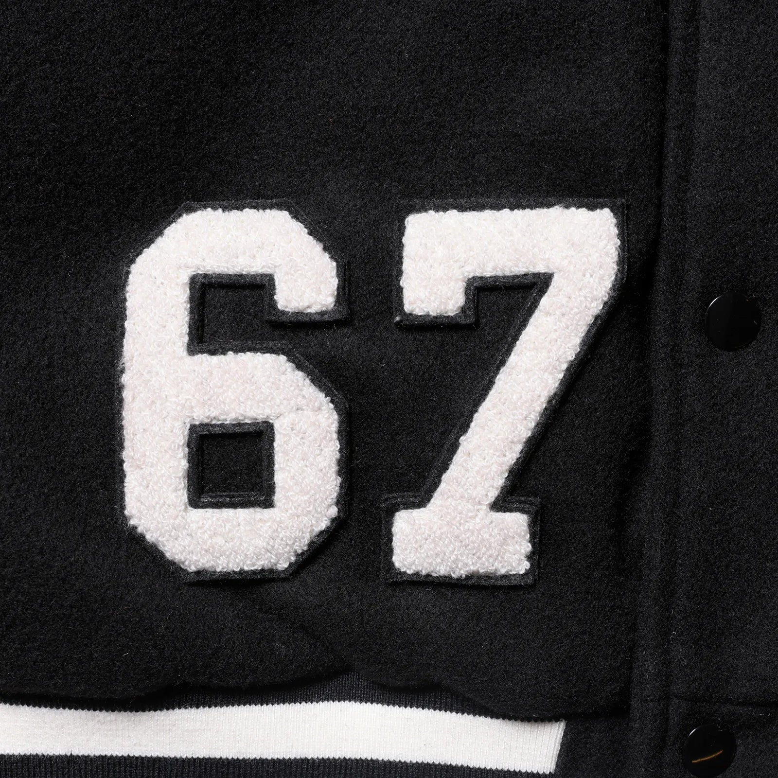 Liberaiders(リベレイダース)の肉厚なバーシティジャケット「LR VARSITY JACKET」のBLACKカラーの正面右下の「67」ワッペンの写真