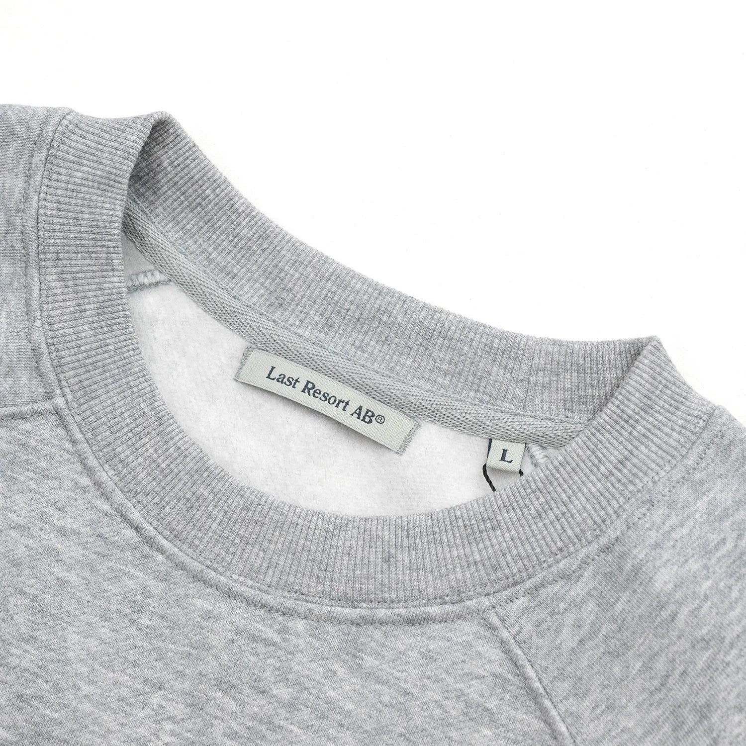 LAST RESORT AB(ラストリゾート)のアトラスロゴが左胸にプリントされたスエット「LITTLE AB RAGLAN CREW SWEAT」の「GREY MELANGED」カラーの襟元の写真