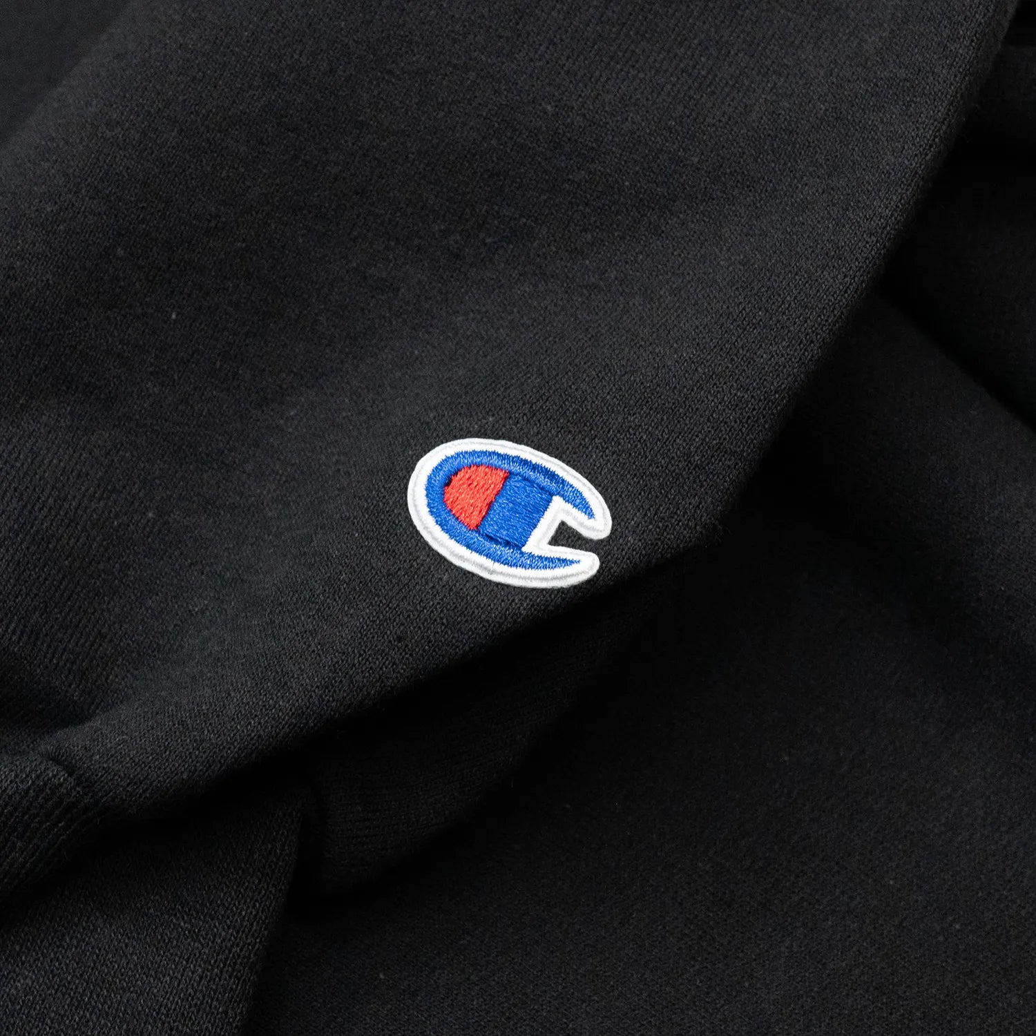 フロントにブランドロゴがフロッキープリントされたPOETS(ポエッツ)のスエット「OG FLOCKED CHAMPION CREW SWEAT」のBLACKカラーの左袖に入ったボディブランドのロゴ写真