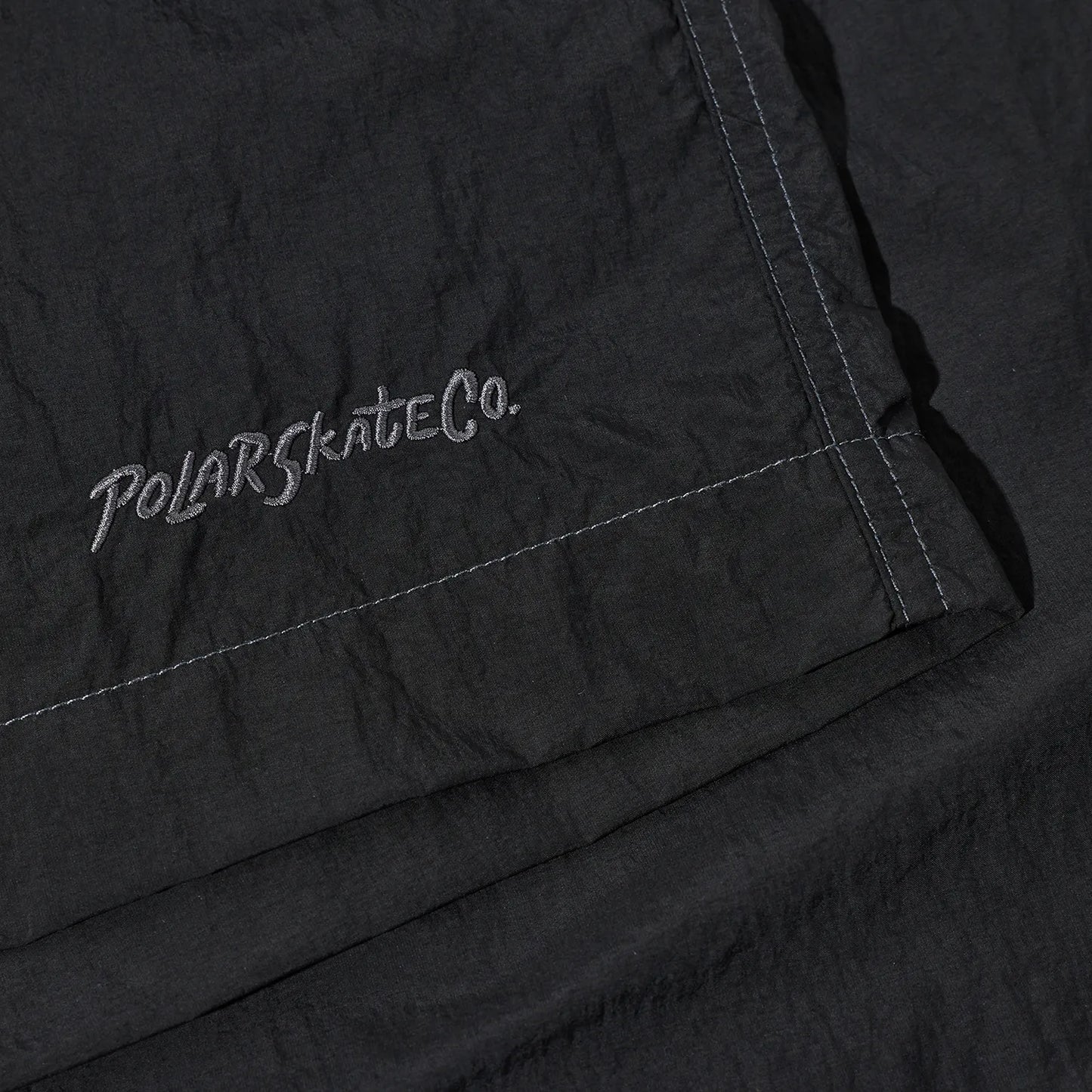 ウエストはバックル仕様で自由にサイズ調整が可能なナイロン生地のPolar Skate Co(ポーラー)のショーツ「HIKE SHORTS」のVINTAGE BLACKカラーの裾の刺繍デザインの写真