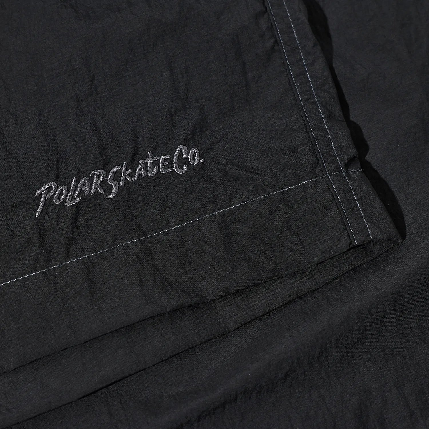 ウエストはバックル仕様で自由にサイズ調整が可能なナイロン生地のPolar Skate Co(ポーラー)のショーツ「HIKE SHORTS」のVINTAGE BLACKカラーの裾の刺繍デザインの写真