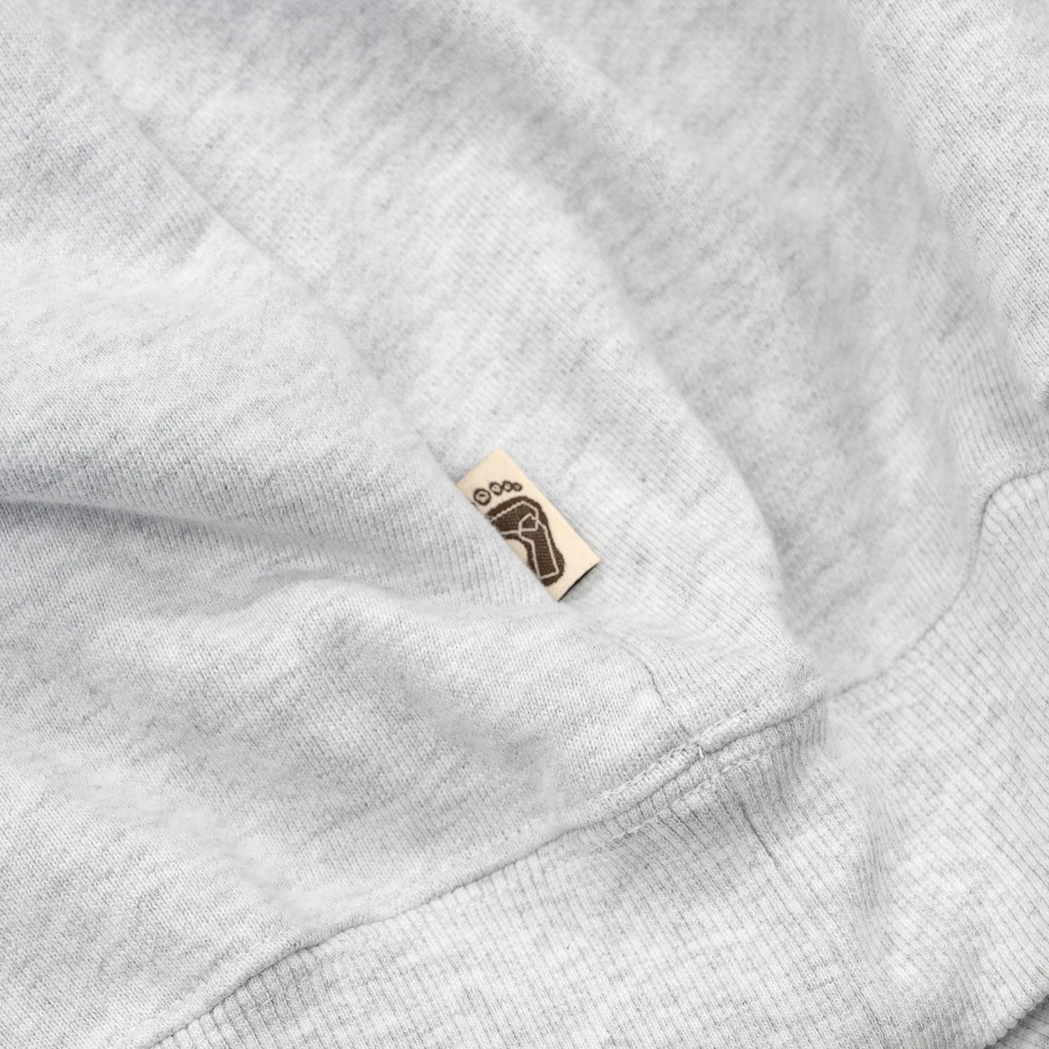 TRIBE WEAR(トライブウェア)の肉厚なフーディー｜パーカー「BASIC HOODIE」のGREYカラーの左脇下のブランドタグ写真