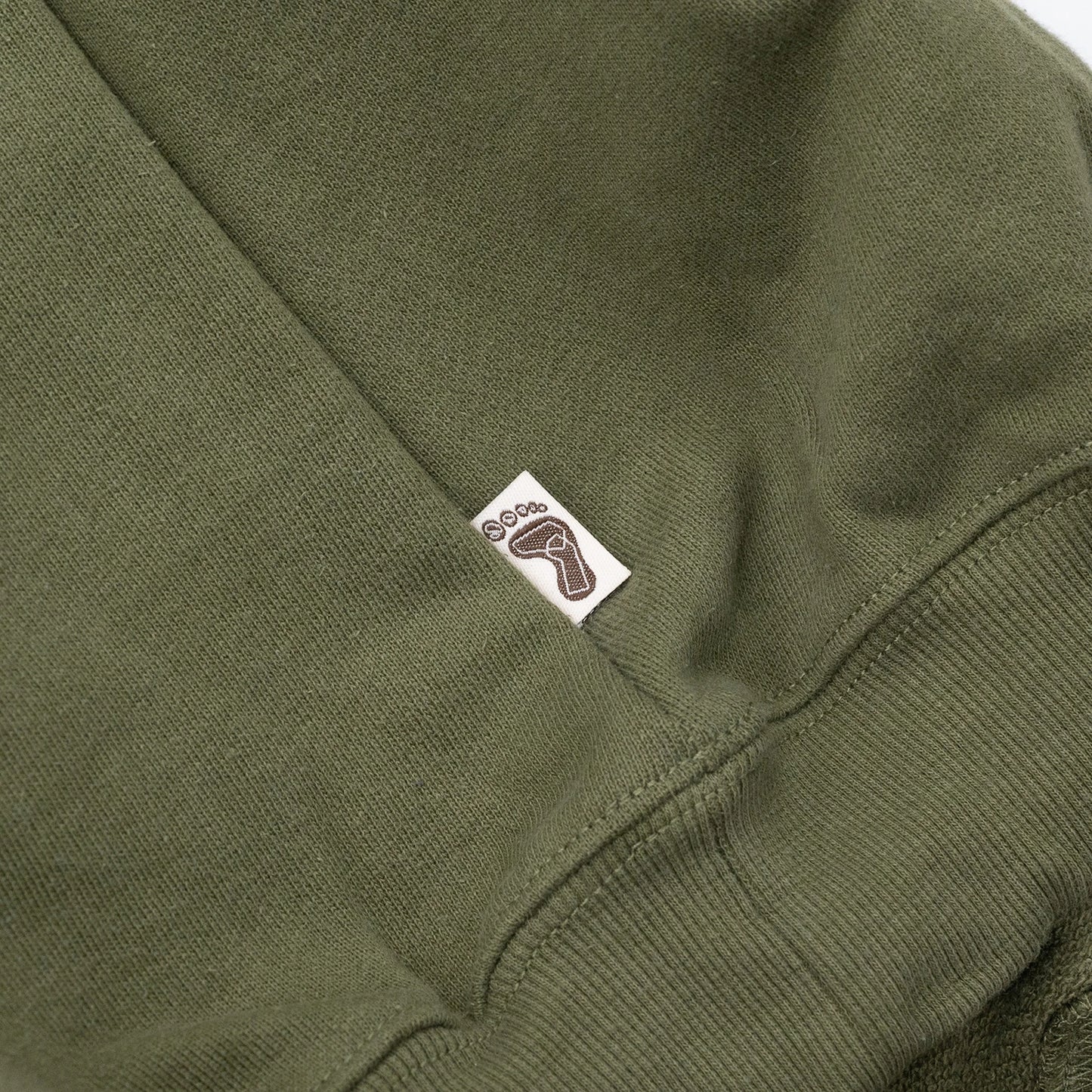 TRIBE WEAR(トライブウェア)の肉厚なフーディー｜パーカー「BASIC HOODIE」のOLIVEカラーの左脇下のブランドタグ写真
