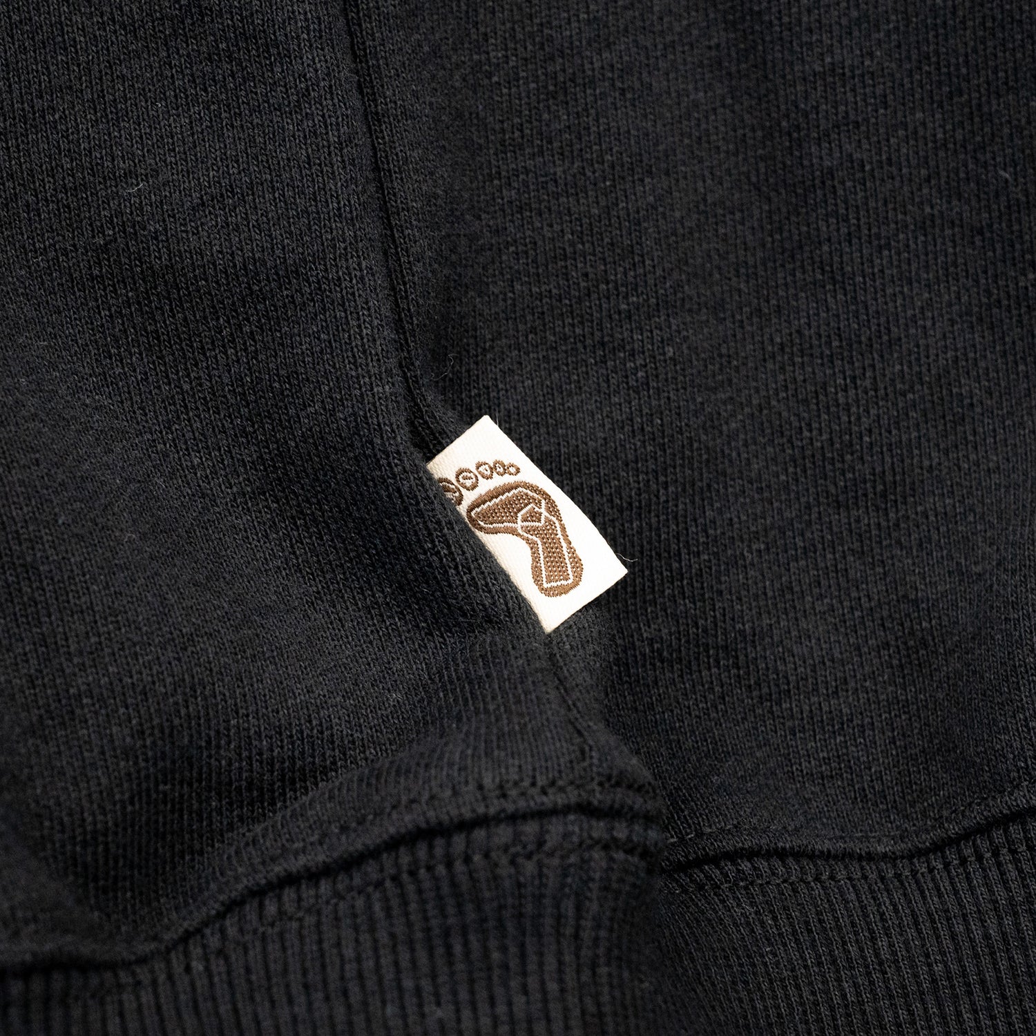 TRIBE WEAR(トライブウェア)の肉厚な生地感とファットなシルエットのクルーネックスエット「BASIC SWEAT CREWNECK」のBLACKカラーの左脇下のブランドタグの写真